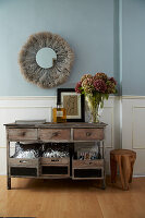 Old sideboard, above it boho mirror on light blue wall