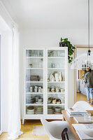 White crockery cupboard, wooden table with shell chairs in the foreground