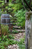 Moosbewachsene Steintreppe, , Holzfaß und rostiges Metall im Garten