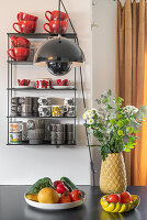 Fruit-vegetable bowl and flower on kitchen counter, in the background wall shelf with dishes