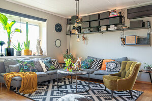 A grey upholstered sofa with cushions, an armchair and a round coffee table on a rug with a geometric pattern