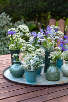 Arrangement aus Schmucklilien (Agapanthus), Kornblumen und Schleierkraut (Gypsophila) in Keramikvasen auf einem Gartentisch