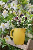 Bouquet of lily of the valley and tulips in a jug in front of azaleas