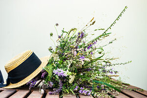 A bouquet of wild flowers and straw hat on wooden table