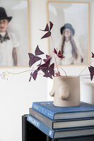 Kunsthandwerkliche Vase mit Blätterzweig auf Bücherstapel, im Hintergrund Kinderportraits