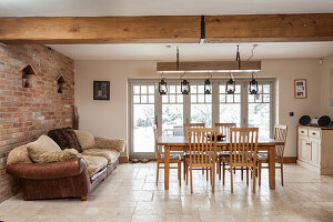 Dining area with wooden furniture and leather couch in front of rustic brick wall