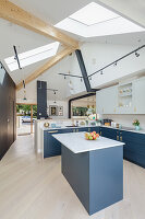 Open kitchen with blue grey cupboard fronts in light living area with skylight