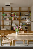 Light wooden dining table with chairs, designer pendant light above, shelves in the background
