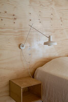 Wall lamp on wooden wall above bedside table and bed