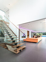 A staircase with a glass balustrade in an open-plan living room with a seating area in the background