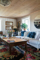 Cosy sofa with cushions, wooden coffee table and kilim rug in rural living room