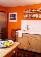 Sammlung von silbernen Teekannen und Geschirr auf Holzregalen über Spülbecken in orangefarbener Küche