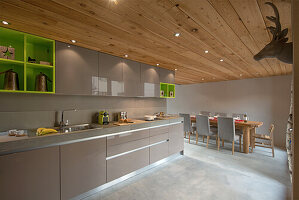 Long kitchen unit in taupe with wooden ceiling, dining area in the background