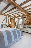 Doppelbett und Sofa in hellen Blau- und Grautönen im Schlafzimmer mit Holzbalkendecke