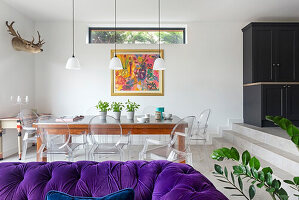 View over purple chesterfield sofa to dining area with transparent chairs in open plan living room