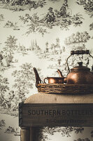 Tea kettle and cup on wicker tray in front of Toile-de-jouy wallpaper