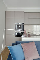 Open living room with blue sofa, built-in kitchen in the background