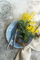 Festive table setting for Easter holiday dinner with bright yellow mimosa flowers on concrete table