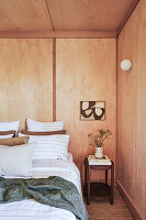 Doppelbett und Nachttisch im Schlafzimmer mit Holzpaneelen