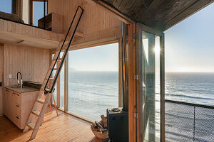 Open kitchen with ladder to the sleeping loft in the wooden house, view of the sea
