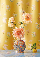 Apricot colored dahlias in a vase in front of a flower curtain