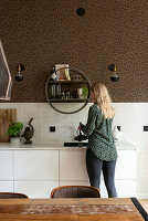 Woman in modern kitchen area with leopard print wall and white cabinets