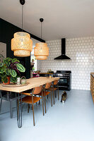 Kitchen with wooden table, retro chairs, rattan pendant lights, white tiles and cat