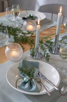 Dining table set with white plates, light blue napkins, fir branches and candle lights