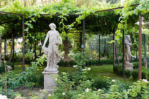 Statuten im Garten und mit Wein bewachsene Pergola