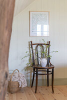 Holzstuhl mit Vase und Zweigen, Korb mit Decke und weiße Wand mit Bild