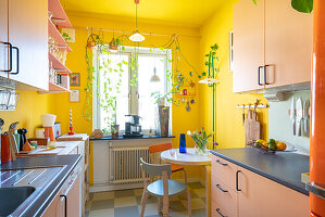 Rosa Schränke und Frühstückstisch in Küche mit gelben Wänden