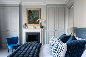 Doppelbett mit blauer Steppdecke aus Samt und  blauer Sessel vor dem Kamin im Schlafzimmer