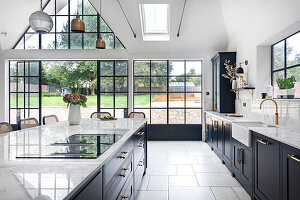 Modern kitchen with cooking island, black cabinets and window front with a view of the garden