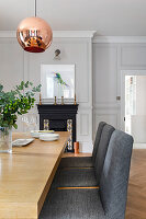 Wooden table and upholstered chairs in dining room with fireplace and copper lamp