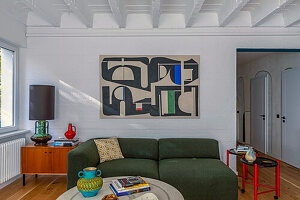 Grünes Sofa, Mid-Century Schränkchen mit Tischlampe und moderne Kunst an der Wand im Wohnzimmer