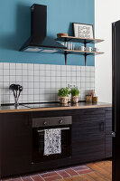 Kitchenette with dark cupboard fronts, above white wall tiles and blue wall