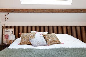 Bed with patterned cushions and wooden bed frame under skylight