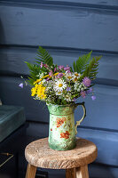 Bunter Wildblumenstrauß in verzierter Vase auf rustikalem Holzhocker