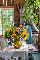 Sommerlicher Blumenstrauß mit Sonnenblumen auf Tisch mit Teekanne und Kerzen in Gartenhaus