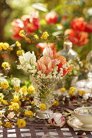 Blumenstrauß aus Tulpen (Tulipa) und Maiglöckchen (Convallaria) in Vase auf Gartentisch