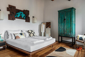 Bedroom with wooden floor, turquoise-colored wardrobe and modern wall lamps