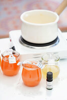 Candle making with colored wax in preserving jars and scented oil on a white table