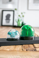 DIY snow globes with green and blue glitter elements on wooden table