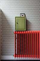 Red radiator and green key box in front of geometrically patterned wallpaper
