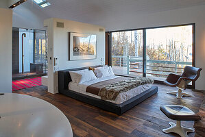 Doppelbett vor Raumteiler im Schlafzimmer mit dunklem Dielenboden und raumhohen Glasfenstern