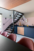 Open-plan kitchen with pink chairs, blue cabinets and black spiral staircase