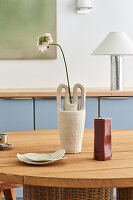 Vase with single flower and red candle on wooden table