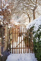 Winterlicher Gartenweg mit Holztor und schneebedeckten Bäumen