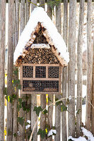 Schneebedecktes Insektenhotel aus Holz an Gartenzaun