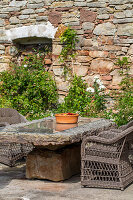 Natural stone table with wicker chairs in front of a brick wall in the garden